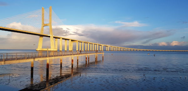 Suspension bridge over river against cloudy sky