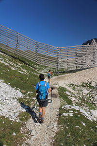 Rear view of hikers walking on land against blue sky