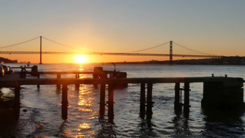 Silhouette bridge over river against sky during sunset