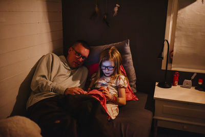 Father with daughter sitting on bed and looking at cell phone