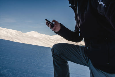 Midsection of man using mobile phone on snow covered mountain against sky