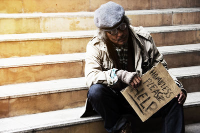 Homeless man holding sign while sitting on steps