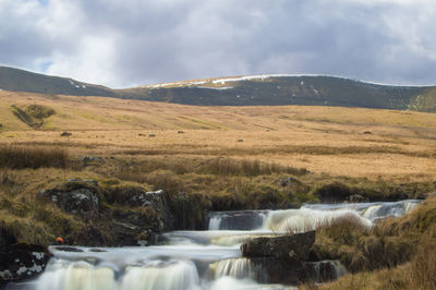 Scenic view of waterfall against cloudy sky