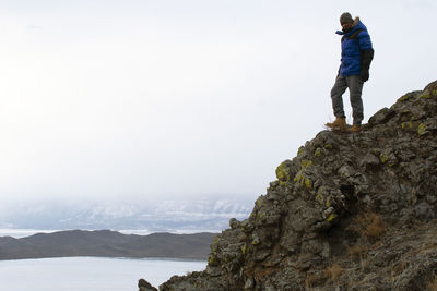 Rear view of man standing on rock against sky