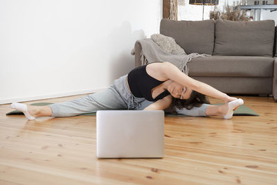 Fit woman doing yoga exercise and watching online tutorials on laptop, training in home living room