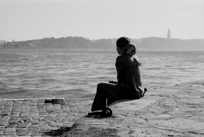 Rear view of boy sitting on shore against clear sky