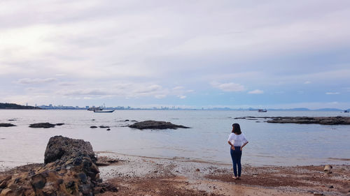 Rear view of woman standing on beach against sky