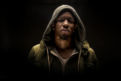 Close-up portrait of serious man wearing hooded short against black background
