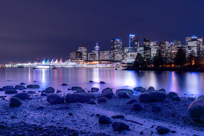 Illuminated cityscape by beach against sky at night