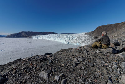 Man looking at view while sitting on land against blue sky