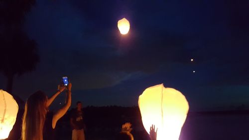 Close-up of hand holding illuminated lights against sky during sunset