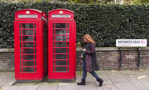 Full length of pregnant woman walking by telephone booths at bayswater road