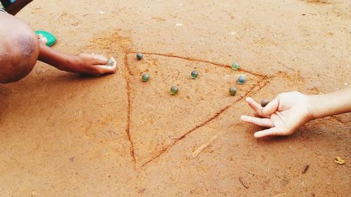 Cropped image of kids playing marbles on dirt