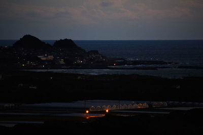 Illuminated city by sea against sky at night