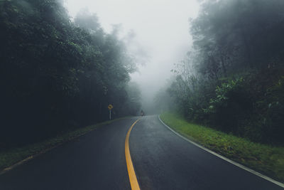 Empty road amidst trees against sky