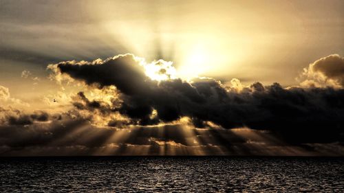 Sunlight streaming through clouds over sea during sunset