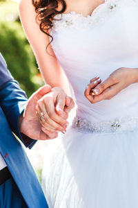Midsection of wedding couple holding hands outdoors