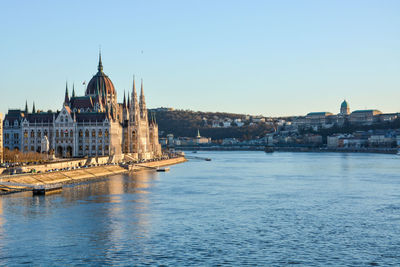 View of buildings by river against clear sky