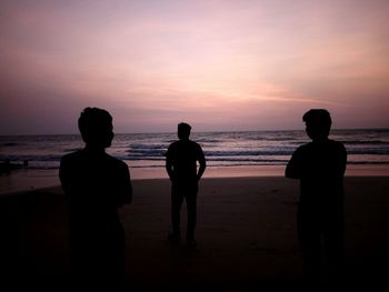 Silhouette people standing on beach against sky during sunset