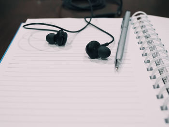 High angle view of in-ear headphones and pen on notebook