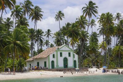 People by palm trees and church against sky