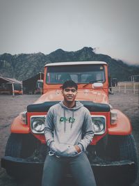 Portrait of young man standing on car against sky