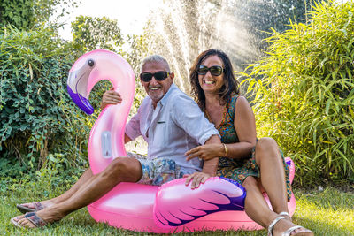 Beautiful smiling middle aged couple having fun sitting on pink flamingo inflatable toy