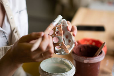 Close up view of female potter wearing apron using glaze brush to paint on pot