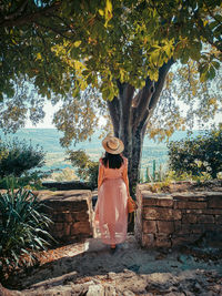 Rear view of woman standing by tree against plants