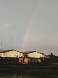 Rainbow over building on field against sky