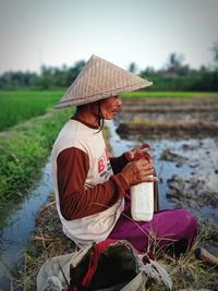 Full length of farmer sitting on field by lake