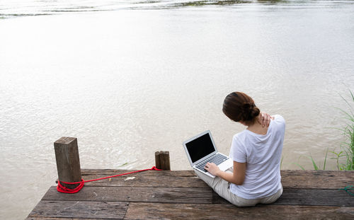 Asian adult woman using computer to work remotely from riverside of rural area