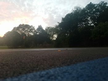 Trees by road against sky during sunset