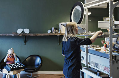 Woman working in eyeglasses workshop with son sitting in background