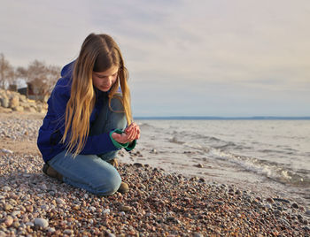 Young adolescent girl collects beautiful colorful rocks, pebbles and shells on the beach