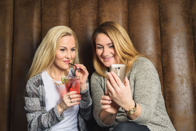 Girlfriends browsing smartphone on sofa in bar