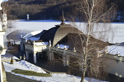 Snow covered houses by trees and buildings against sky