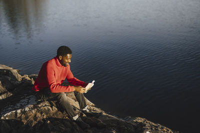 Man reading book while sitting on rock during weekend