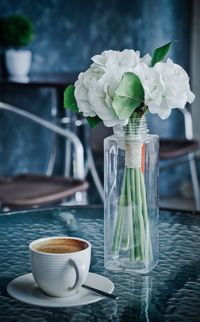Coffee cup and white rose in vase on table