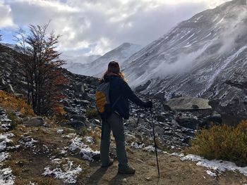 Rear view of man standing on snowcapped mountain against sky