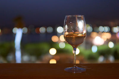 A glass of white wine with bokeh lights in the background and dark sky