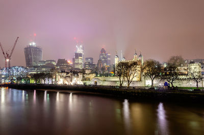 Illuminated buildings by river against sky in city at night