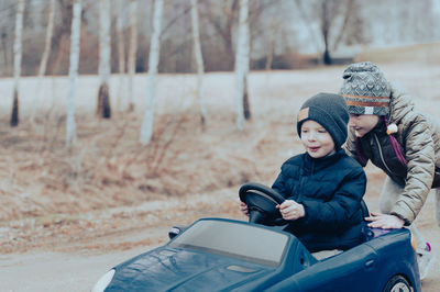 Two happy children playing with big old toy car in countryside, outdoors.