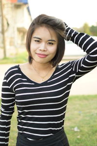 Portrait of smiling young woman with hand in hair standing at park