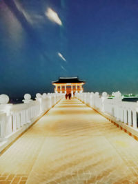 Illuminated footpath amidst buildings against sky at night