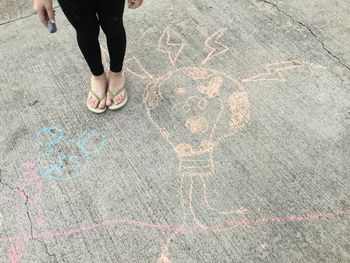 Low section of woman standing by chalk drawing on street