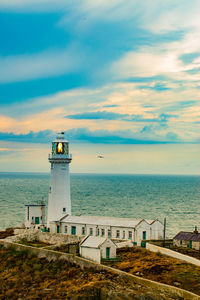 Lighthouse amidst sea and buildings against sky