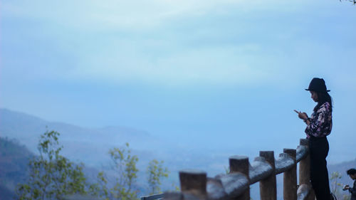 Man standing by railing against sky