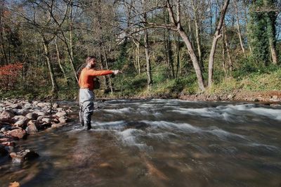 Man fishing while standing in river at forest