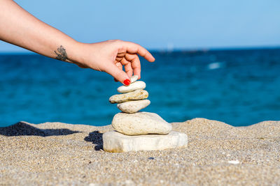 Cropped hand of woman stacking stones at beach against sea